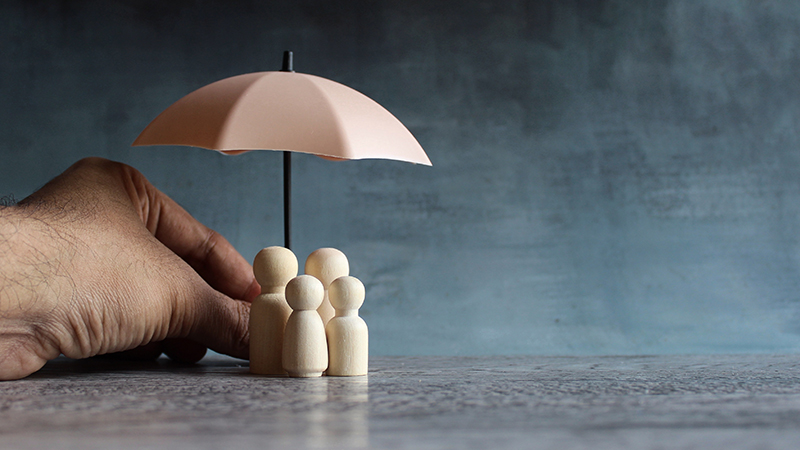 Hand protecting wooden family figures under umbrella – symbolizing builder’s risk insurance near Oshawa