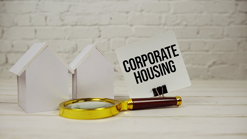 Magnifying glass and paper houses next to “Corporate Housing” sign – illustrating temporary construction insurance in Ontario